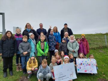 Etwa 20 Kinder zeigen am Deich Plakate mit der Spendensumme und Bildern von Tieren und Natur. Vier Erwachsene freuen sich über die Aktion der Kinder.